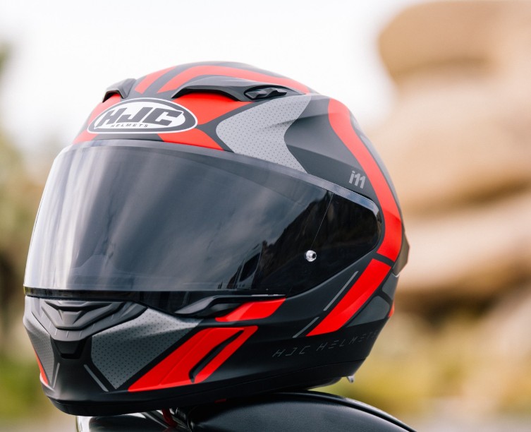 HJC i11 full-face helmet in red and black with clear visor displayed outdoors