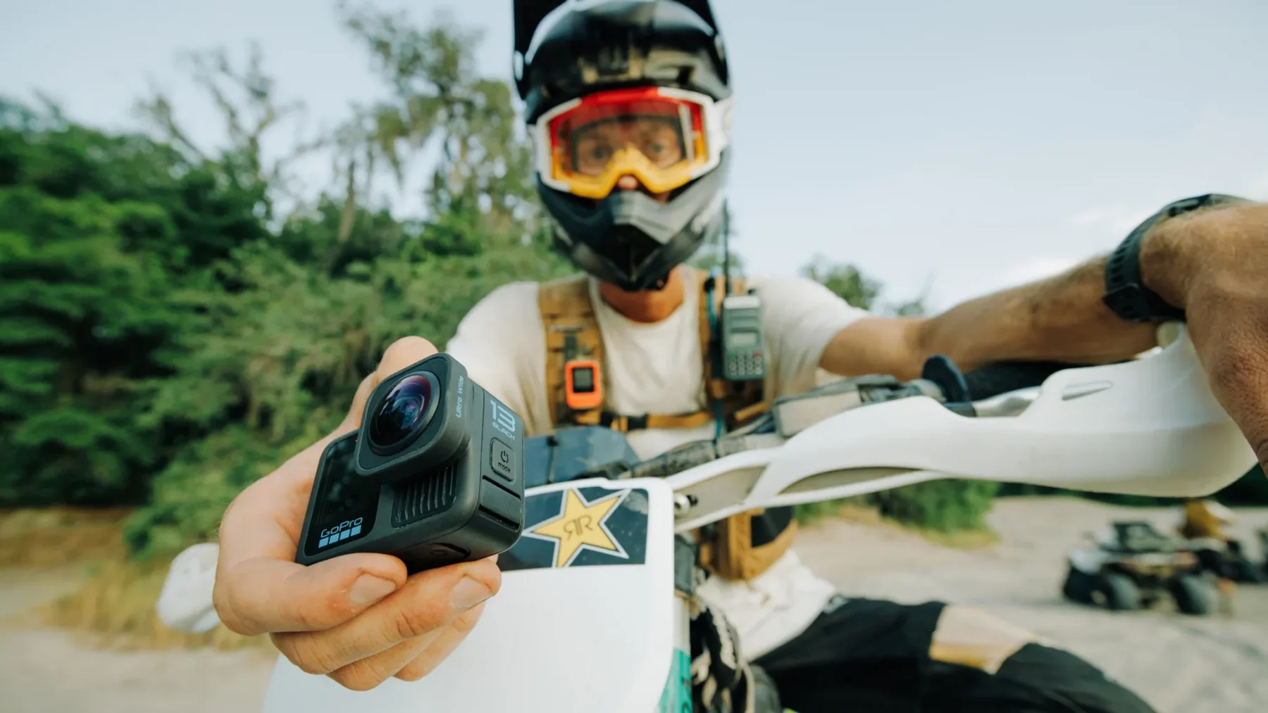 Motocross rider holding a GoPro HERO13 Black action camera while seated on a dirt bike
