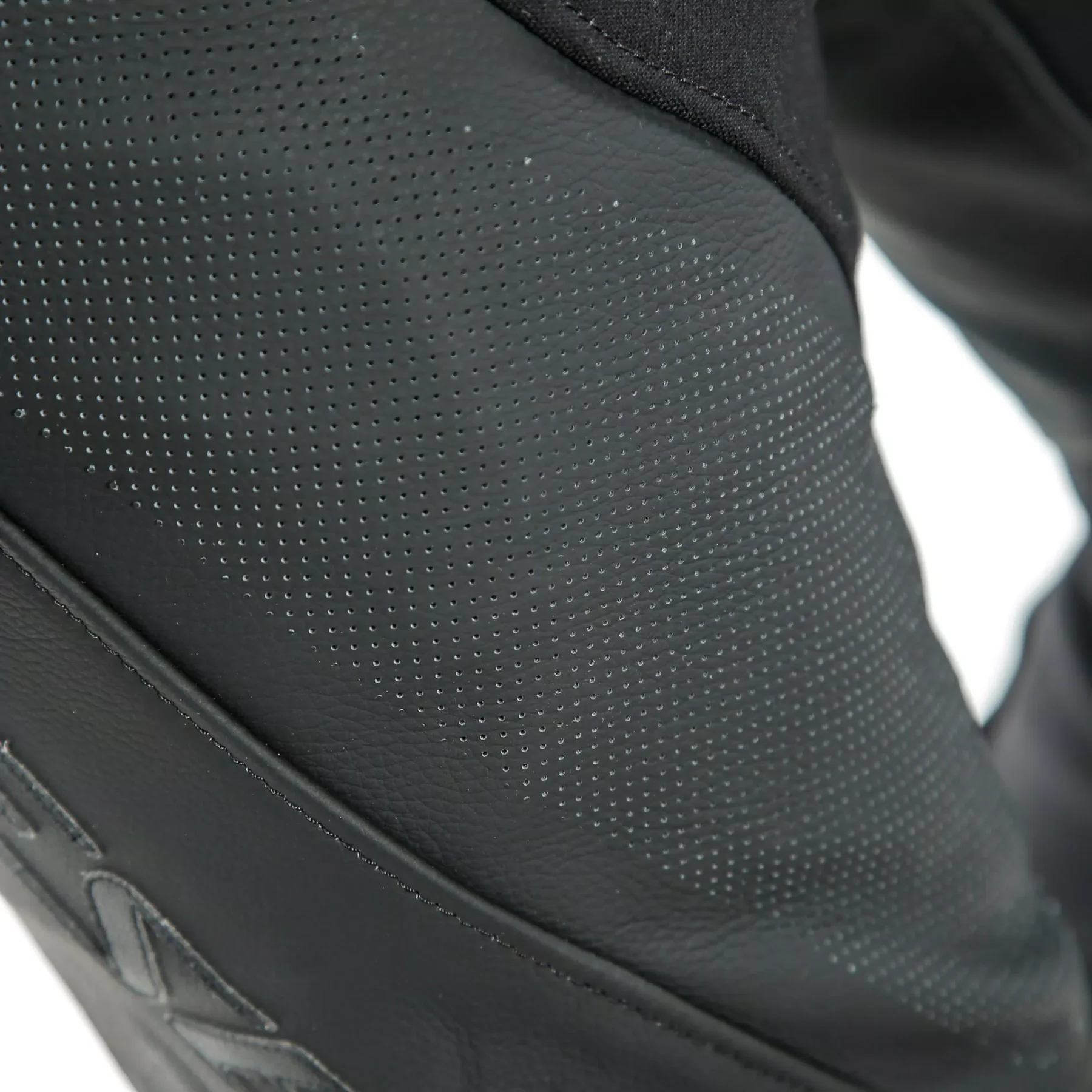 Close-up of perforated black leather motorcycle pants showing ventilation holes for airflow.