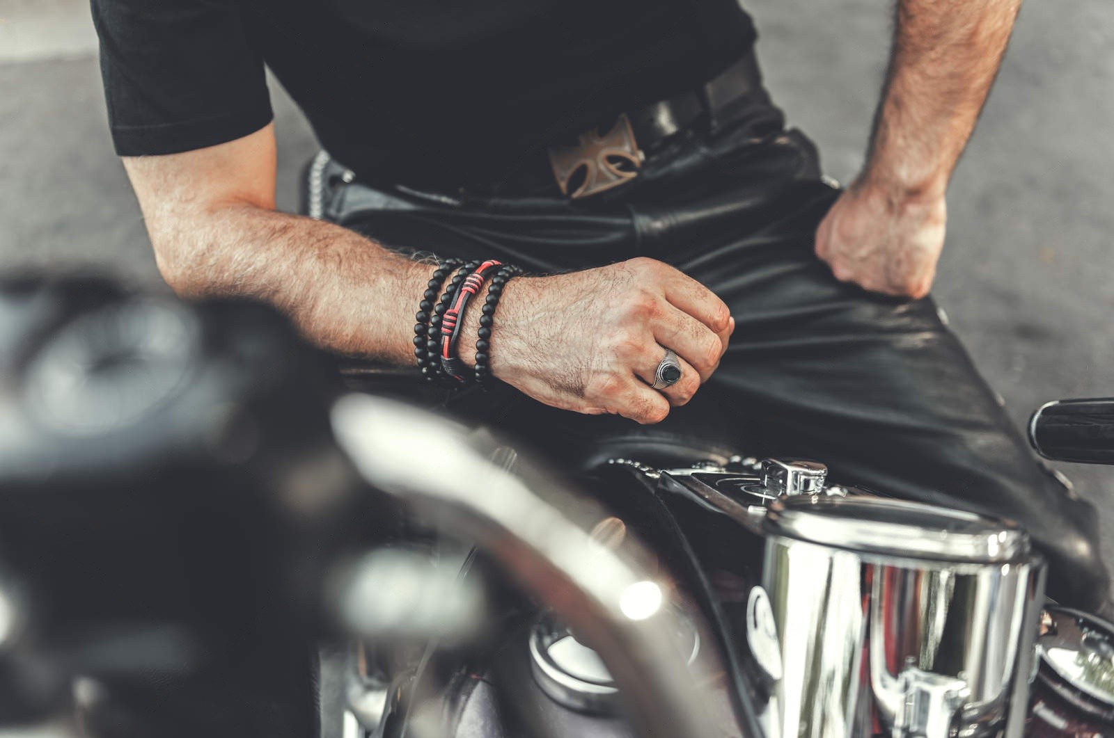 Close-up of a biker wearing black leather pants and accessories while sitting on a motorcycle.