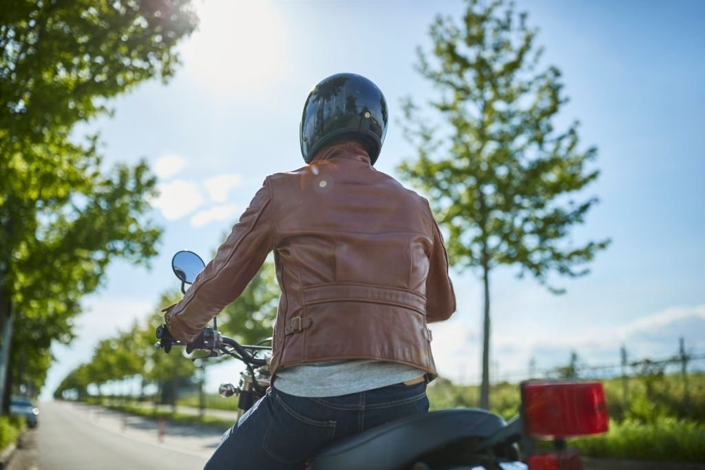 Motorcyclist seated in riding position wearing a snug leather jacket and helmet, viewed from the back