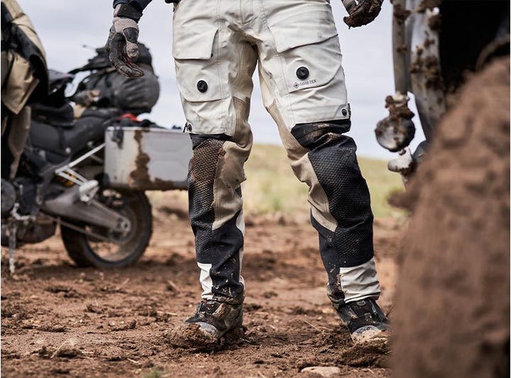 Rider standing in REV'IT! Dominator 3 GTX pants, covered in mud during off-road touring