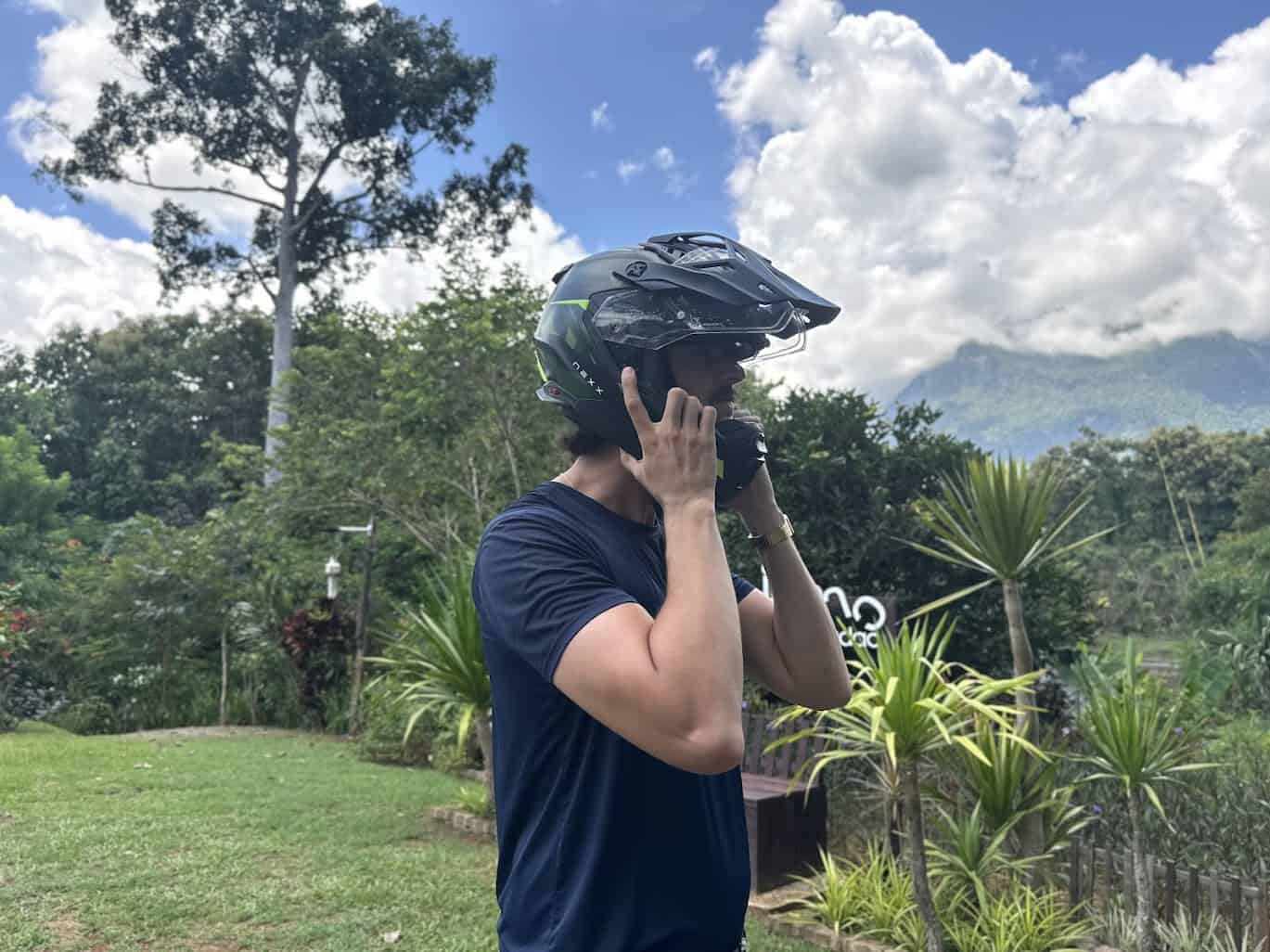 Rider wearing the Nexx X.WED3 helmet in a lush outdoor setting, adjusting the chin strap