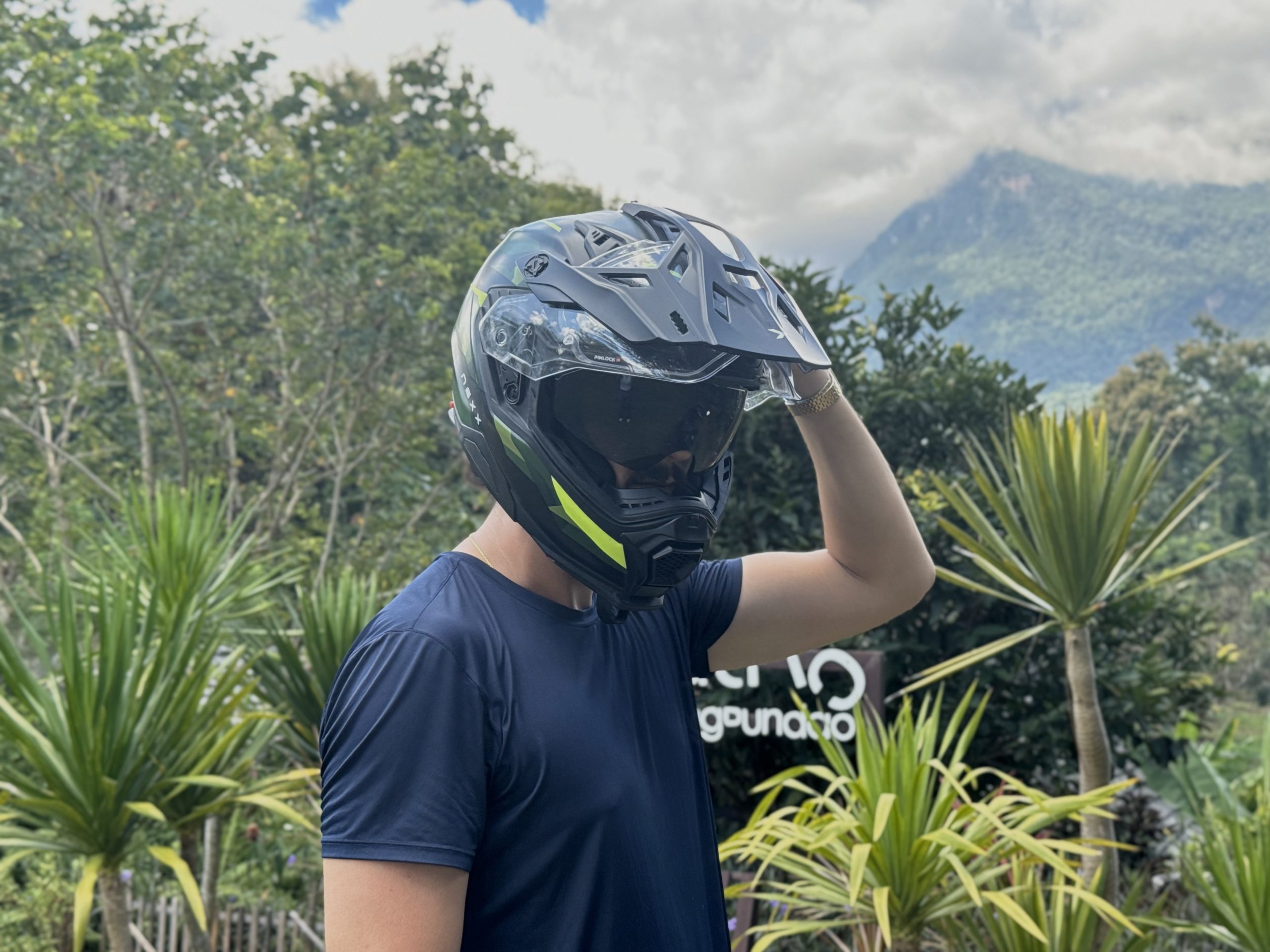 Motorcyclist wearing a full-face helmet and camouflage jacket standing beside a motorcycle