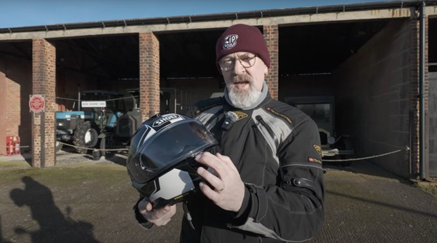 Rider holding Shoei GT-Air 3 helmet, pointing to the new center visor tab