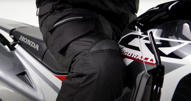 Rider wearing black motorcycle pants with visible knee reinforcement and cargo pocket while seated on a sport bike