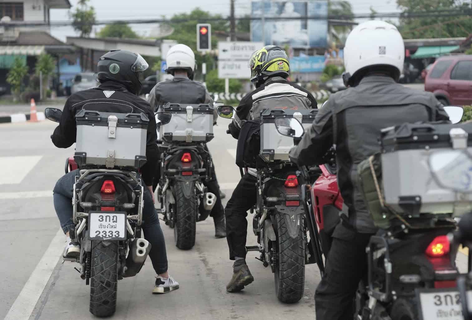 Group of motorcycle riders at a traffic light wearing various textile and leather riding jackets with luggage cases