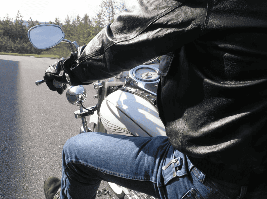 Motorcyclist wearing jeans and leather jacket on cruiser, showcasing riding posture fit