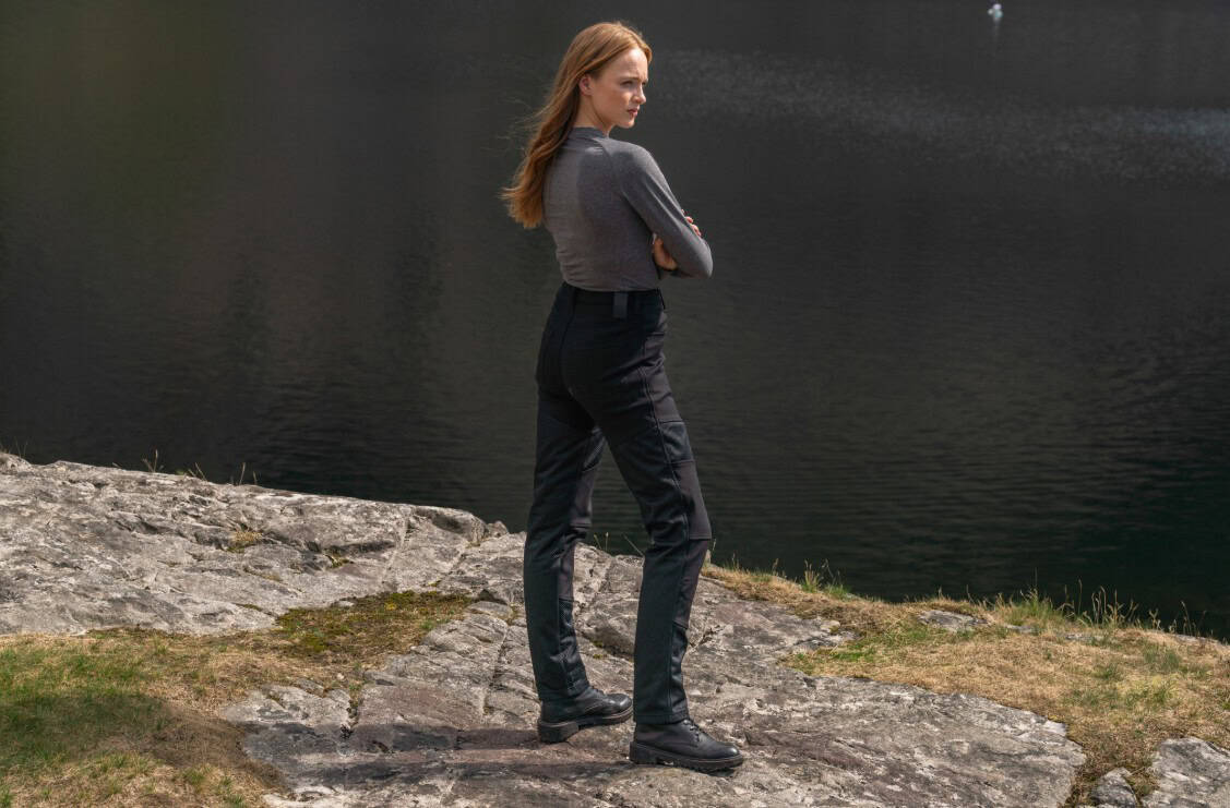 Woman standing outdoors in sleek black motorcycle pants, blending riding gear with casual style