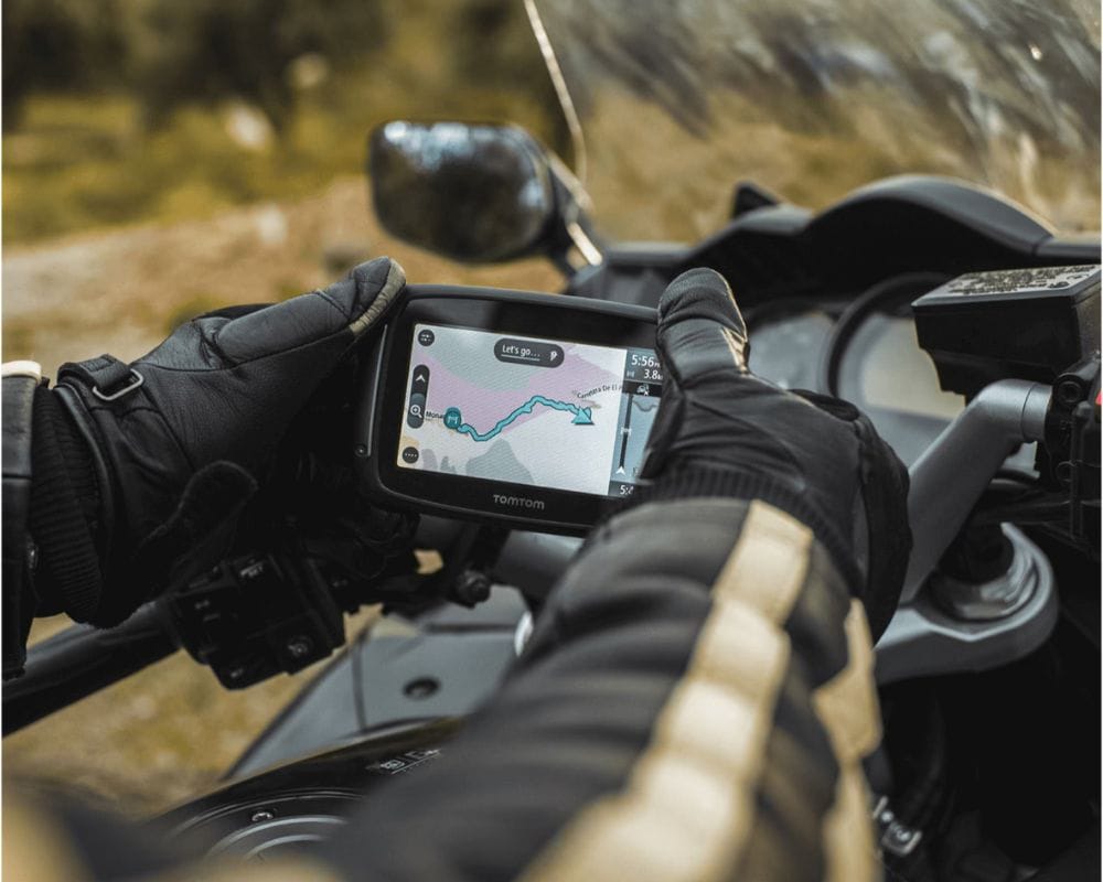 Motorcyclist using a standalone TomTom Rider 550 GPS unit with gloved hands on a touring bike