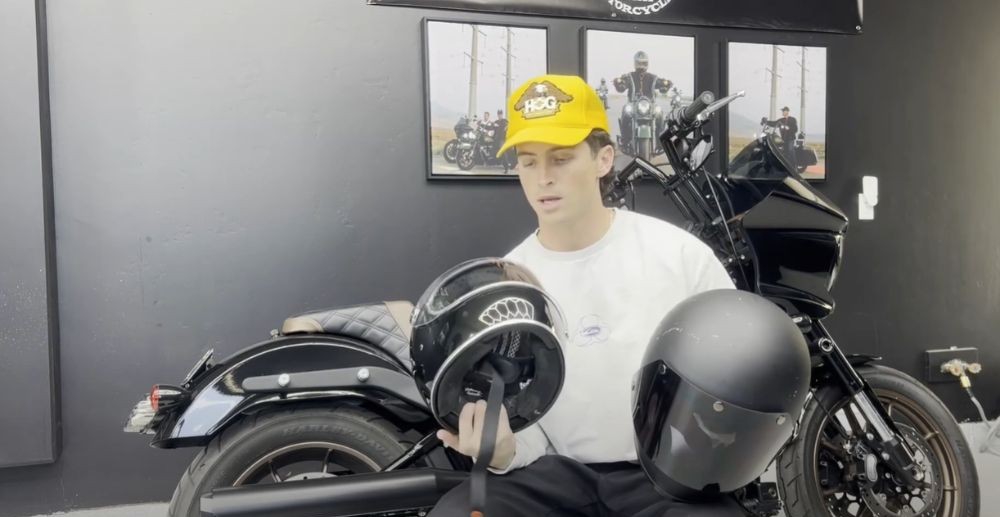 Rider holding both the Biltwell Gringo and Gringo S helmets side by side in a garage setting with a black motorcycle in the background.
