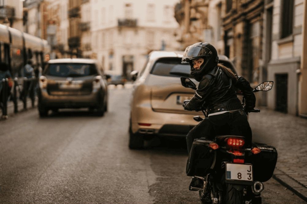 Woman in motorcycle gear riding through city traffic