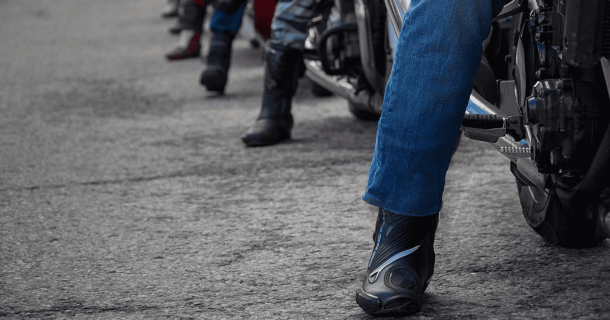 Motorcyclists wearing protective riding boots, showing different styles lined up on a city street.