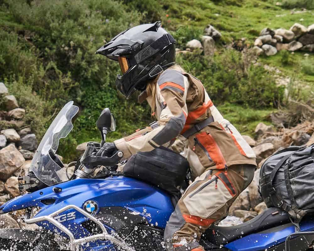 Female adventure rider splashing through water on a dual-sport bike wearing Klim Artemis gear.