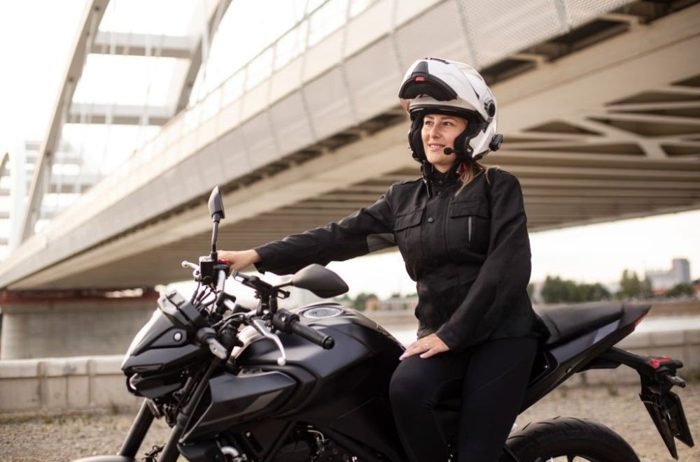 Woman sitting sideways on motorcycle in full riding gear, smiling under helmet