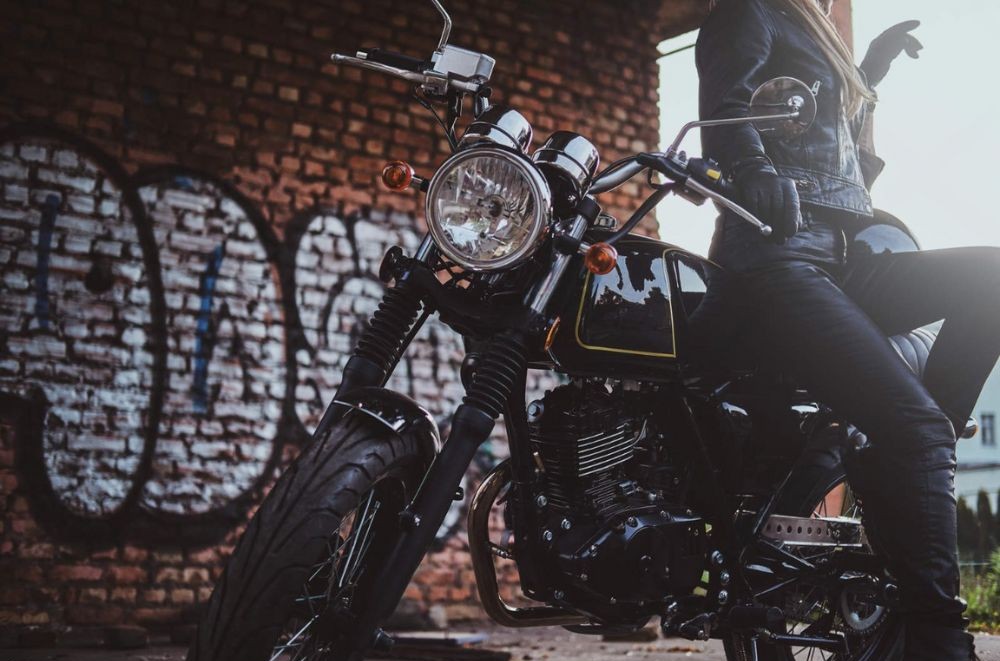 Woman wearing black leather motorcycle pants and boots, seated confidently on a bike in an urban setting