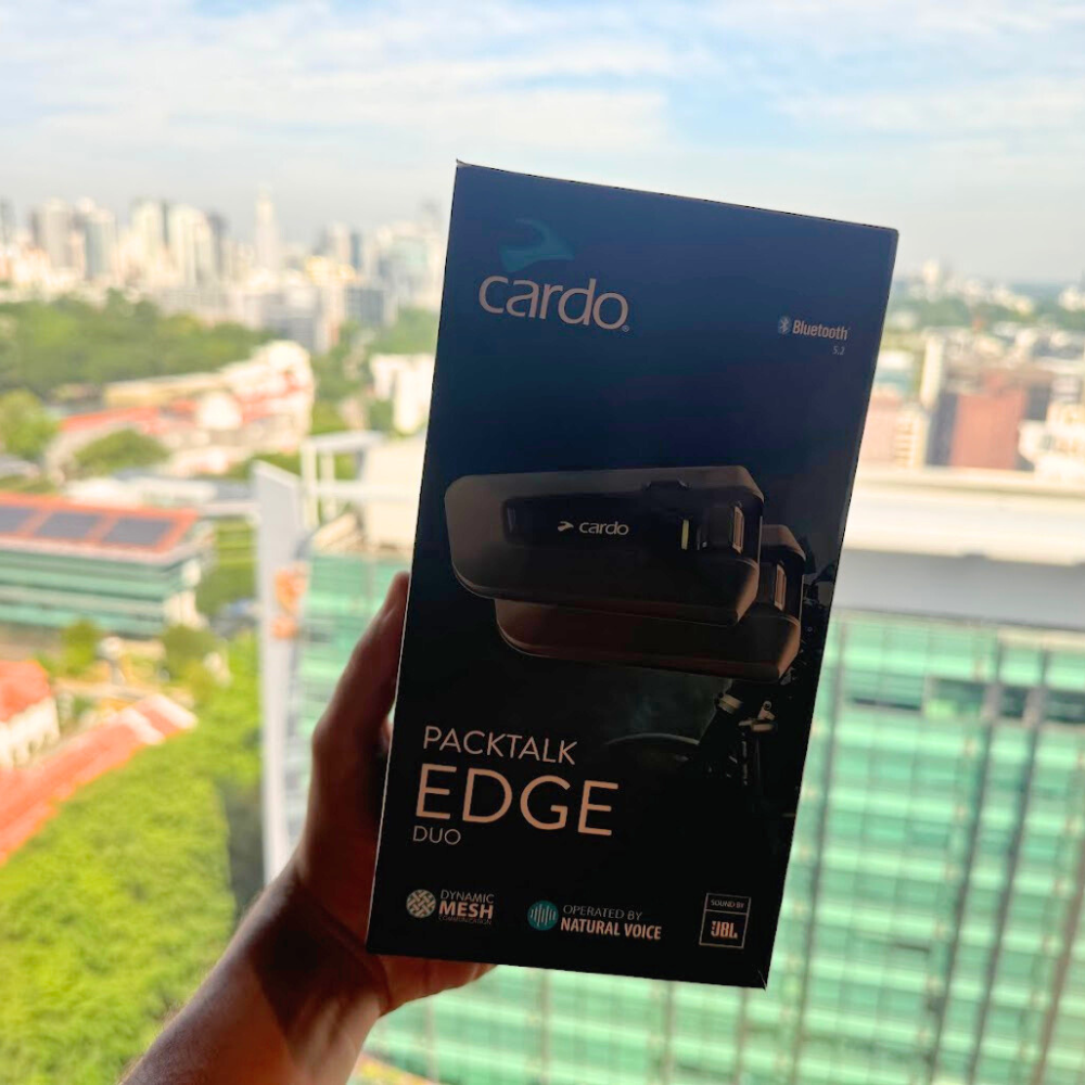 Hand holding Cardo Packtalk Edge Duo box with city skyline in the background