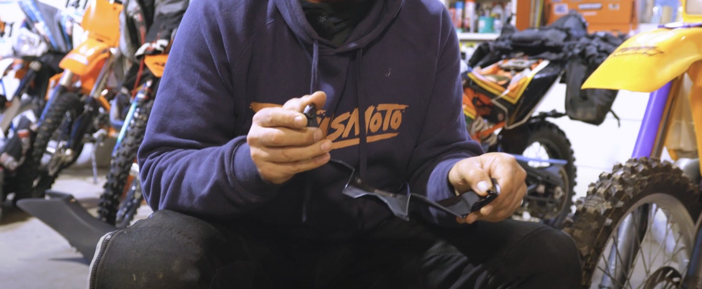 Close-up of hands holding broken Moto-10 helmet visor lugs in a workshop