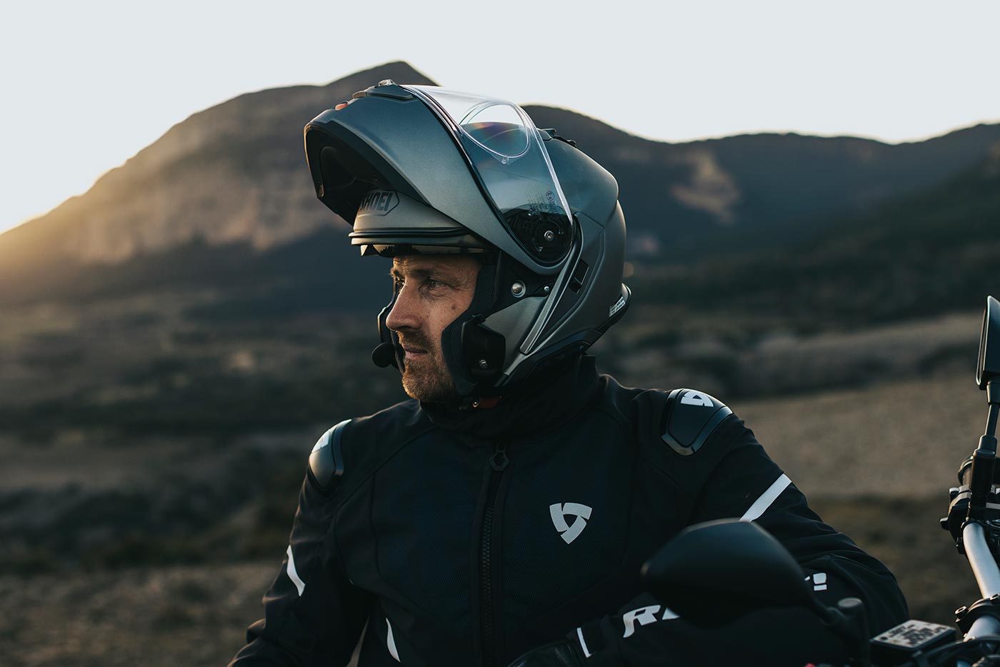 Rider wearing a Shoei Neotec 3 with chin bar raised, taking in mountain scenery