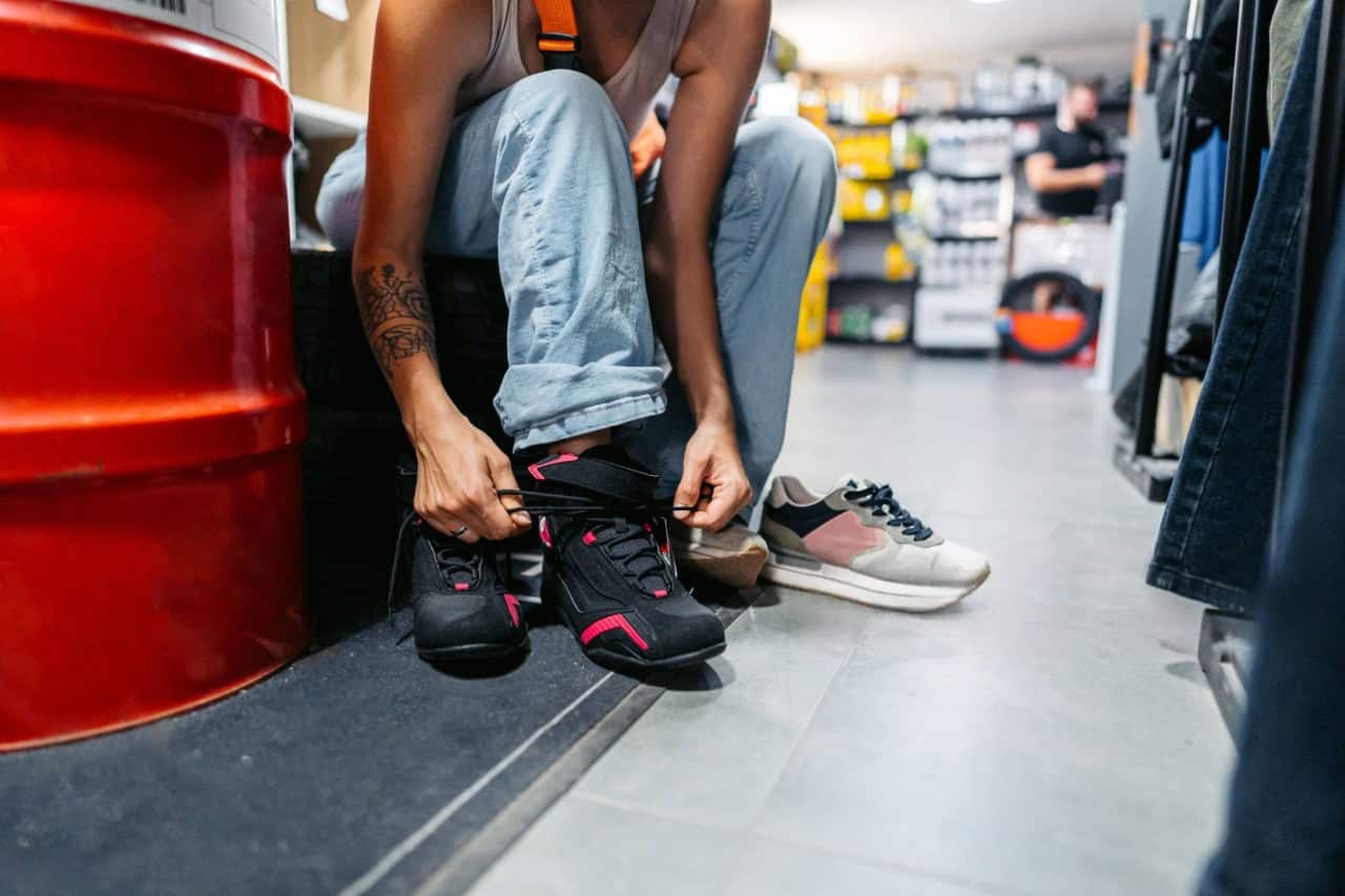 Person trying on motorcycle riding shoes, comparing fit with casual sneakers.