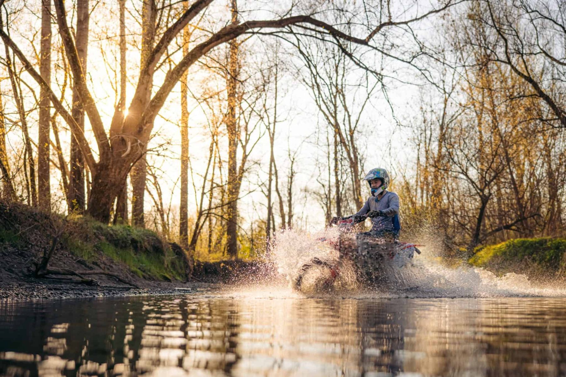 Motorcyclist riding through water on a forest trail, showcasing real-world waterproof gear use