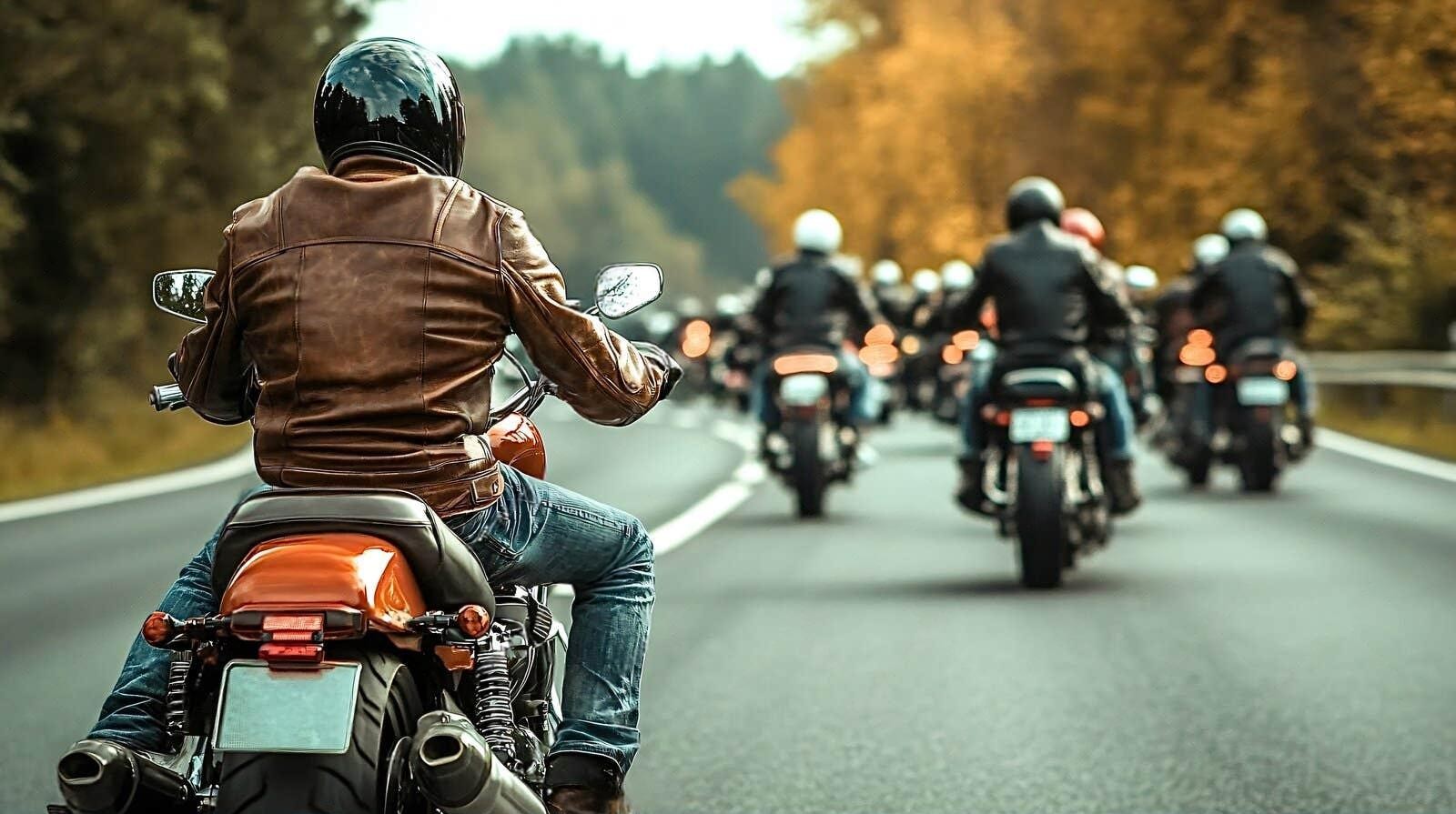Group of motorcyclists riding on a scenic road, with rider in a brown leather jacket in the foreground