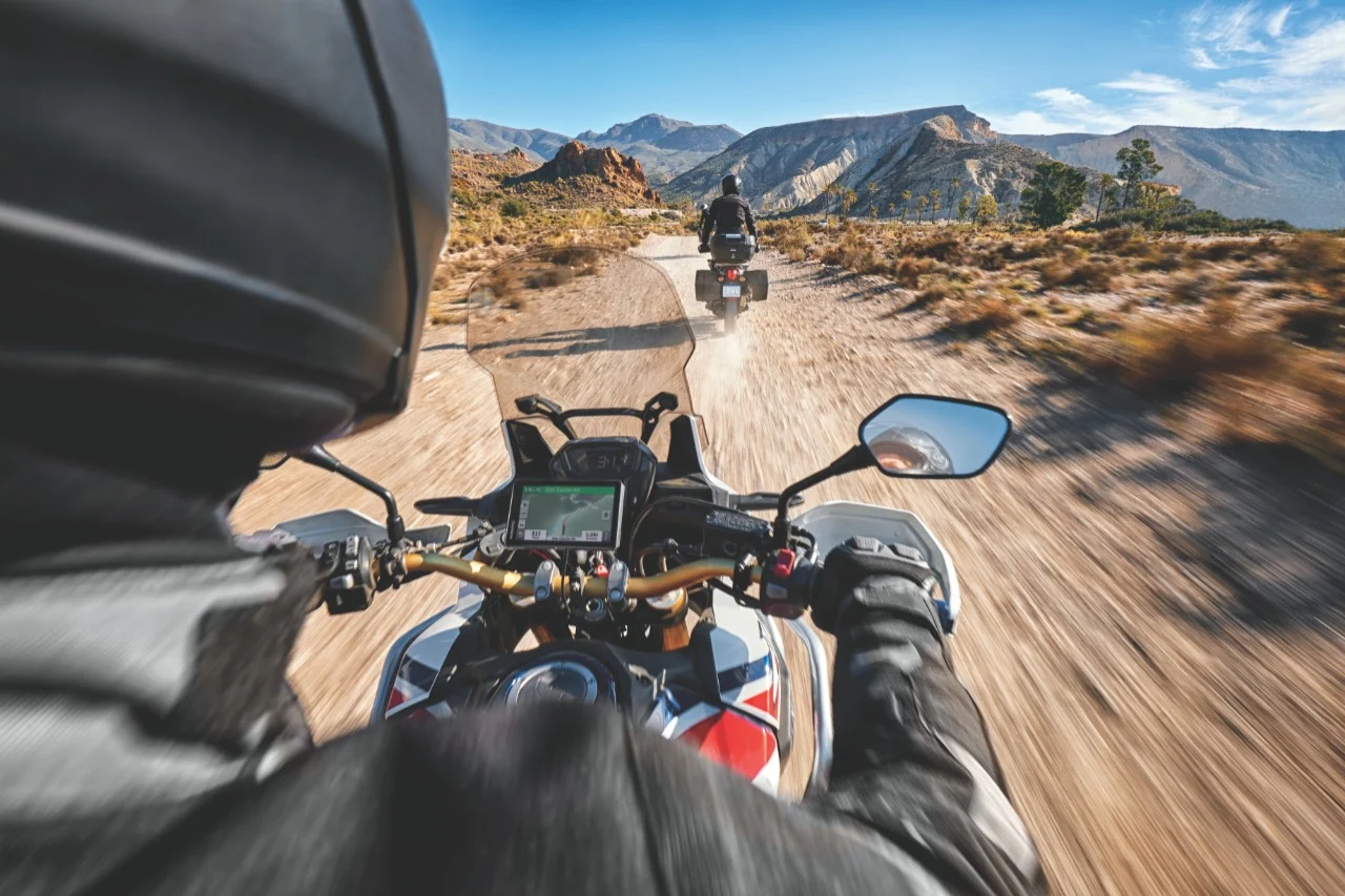 Adventure riders on a dirt trail using GPS navigation with rugged handlebars and windscreen setup