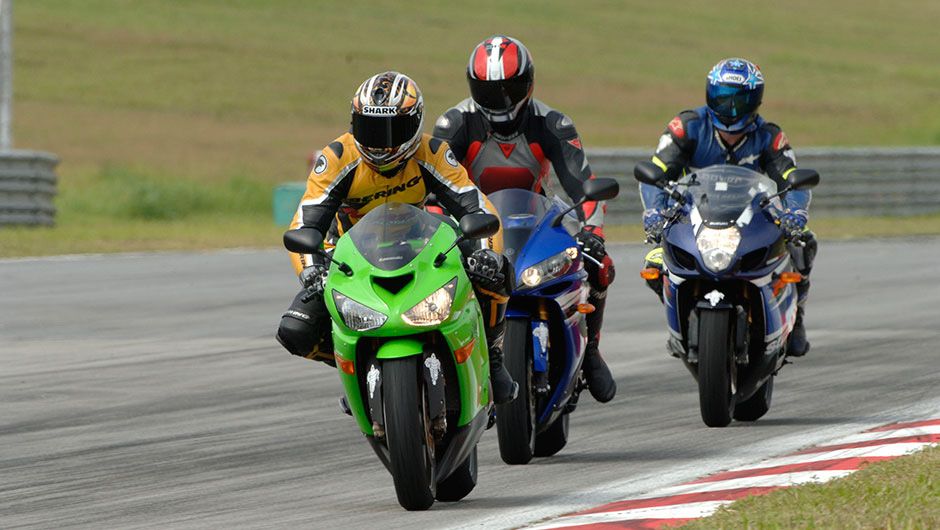 Three sportbikes with riders in racing gear riding on a track side by side
