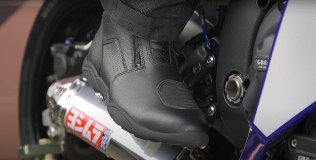 Close-up of a rider wearing BILT Pro Tourer Air Boots on a motorcycle footpeg, showing perforated upper and shift panel in a riding position.