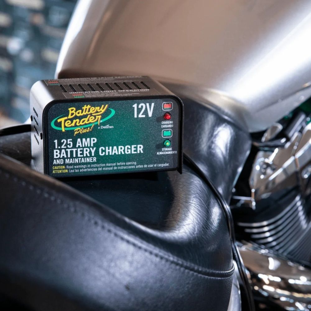 Battery Tender Plus 1.25A charger resting on a motorcycle seat, ready for use.