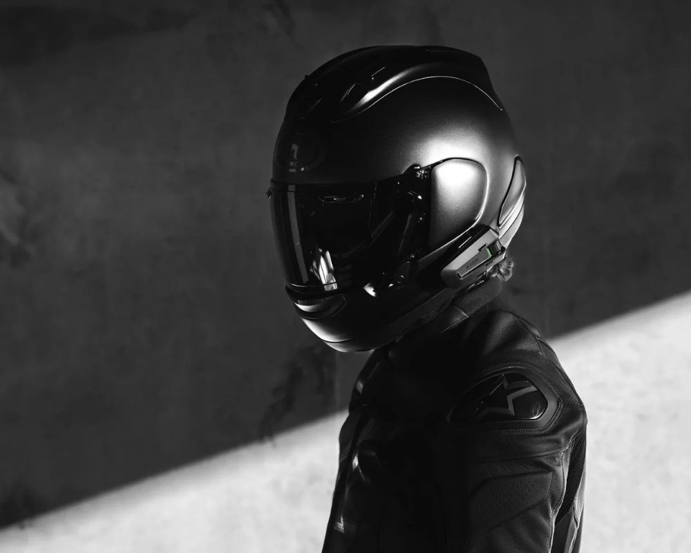 Rider in black gear wearing a full-face helmet with the Cardo Packtalk Pro communicator installed on the side