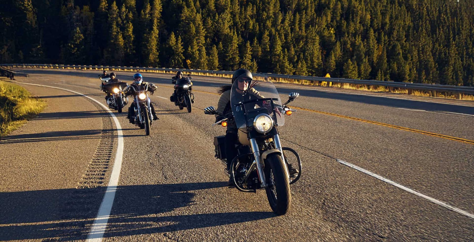 Motorcyclists riding in a group with half helmets on a scenic highway, representing freedom and modern comms integration