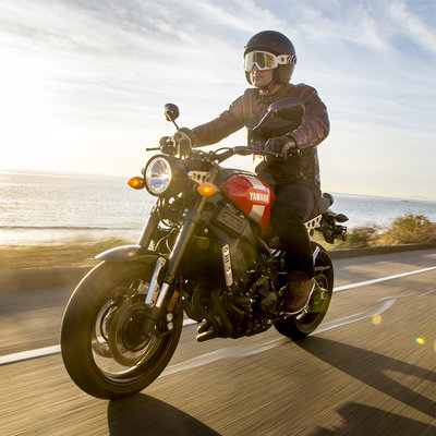 Motorcyclist wearing an open-face helmet riding along a coastal road in warm weather, enjoying the breeze and sunset