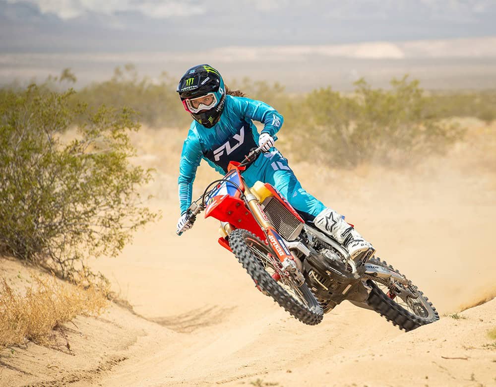 Female rider wearing Fly Racing Lite women’s motocross pants while riding a dirt bike in sandy terrain