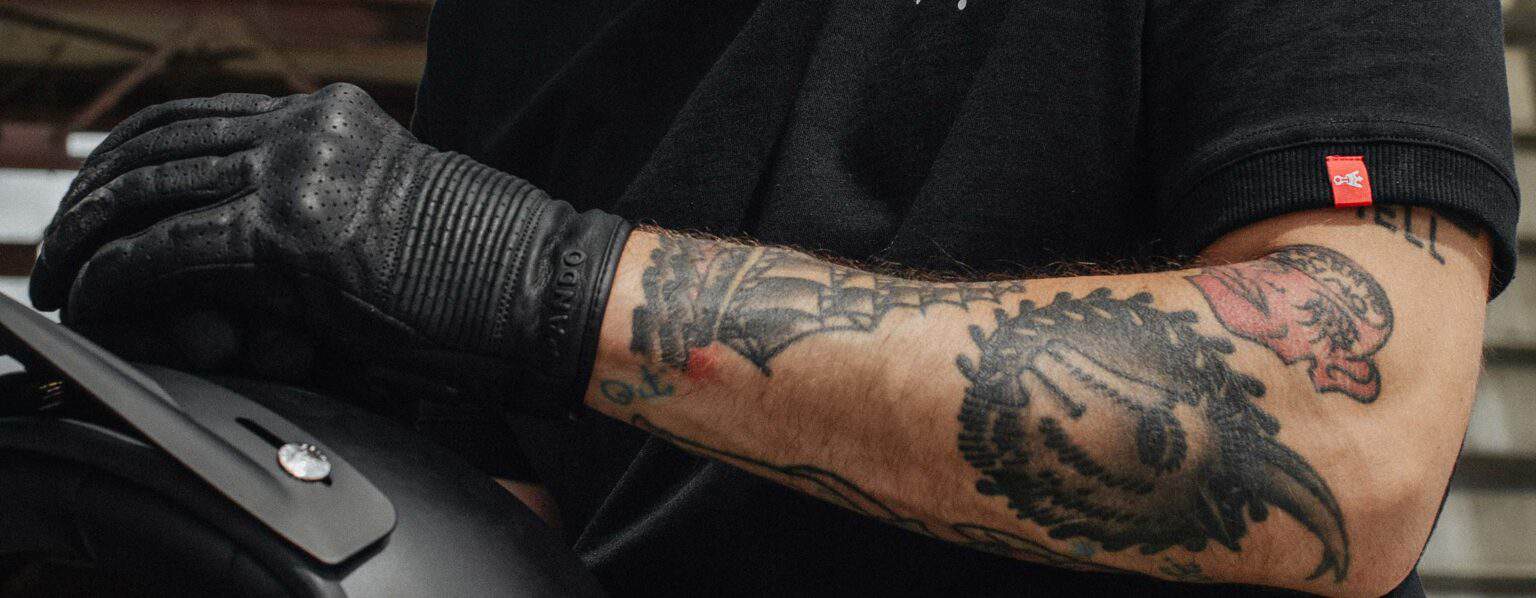 Close-up of a tattooed rider wearing perforated black leather gloves with hidden protection.