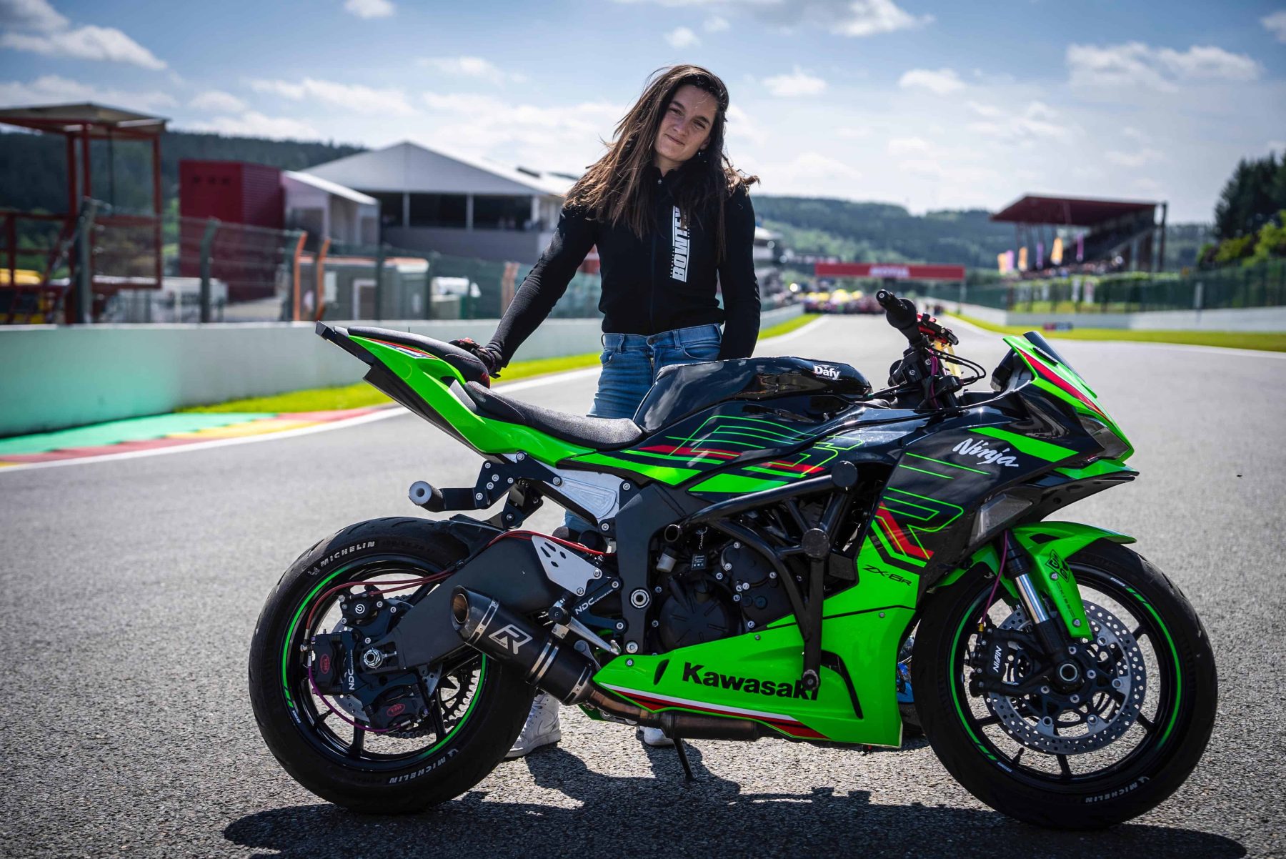 Woman standing next to a Kawasaki Ninja ZX-6R motorcycle on a racetrack