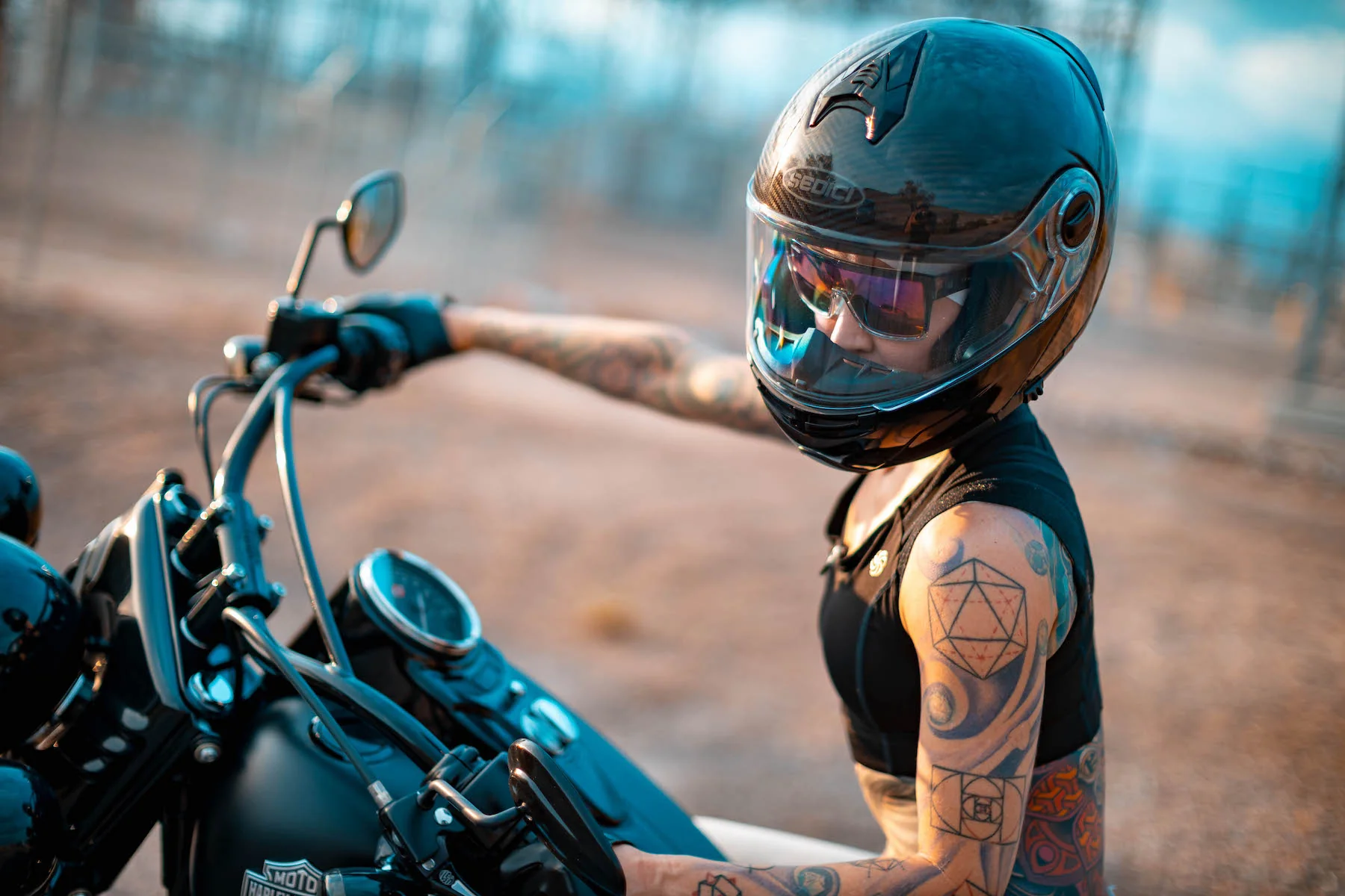 Tattooed rider wearing sunglasses under a full-face helmet while sitting on a cruiser motorcycle