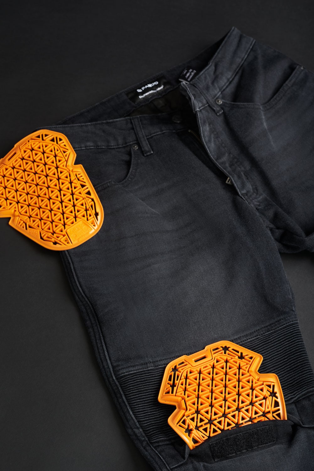 Close-up of black motorcycle jeans with visible orange SAS-TEC armor pads in knee and hip areas