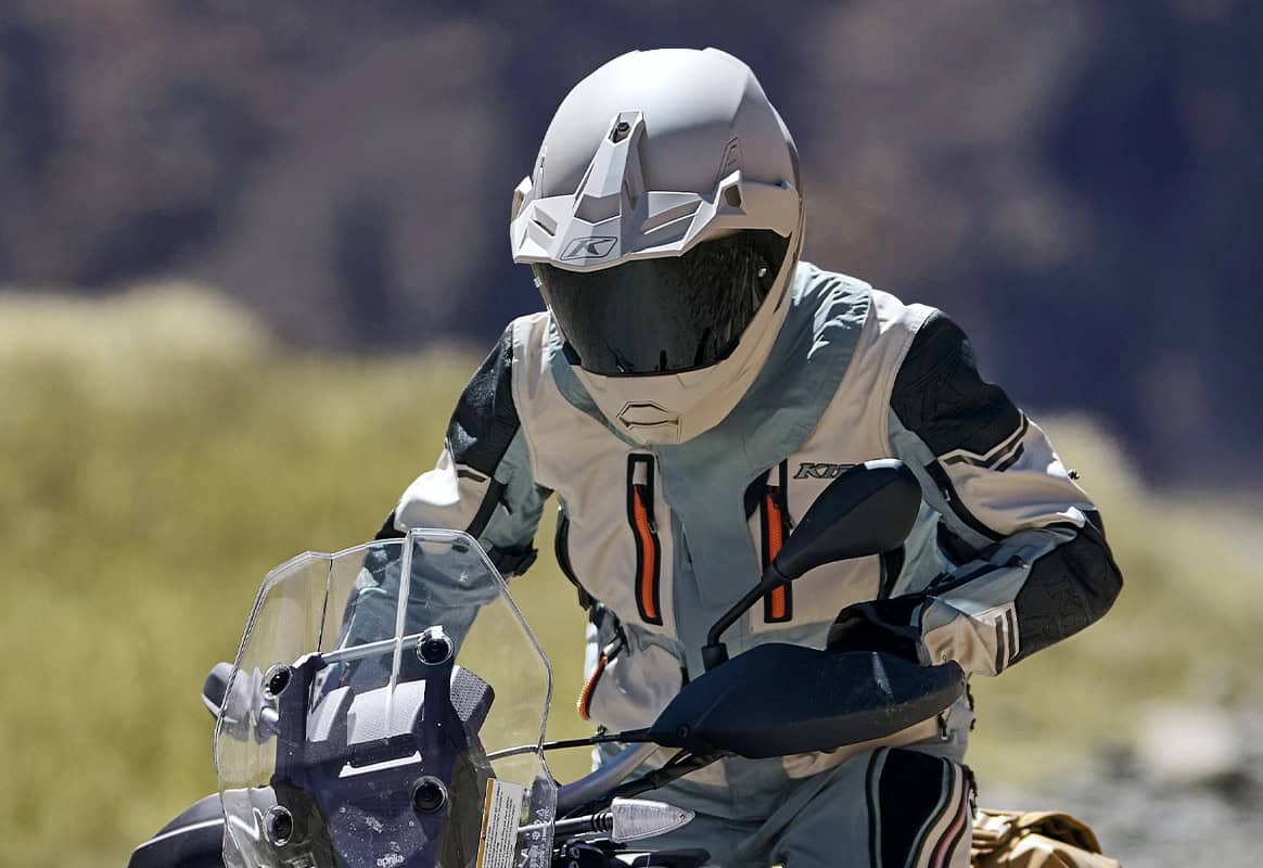 Adventure motorcyclist wearing a Klim jacket and helmet, riding through rugged terrain on a touring bike