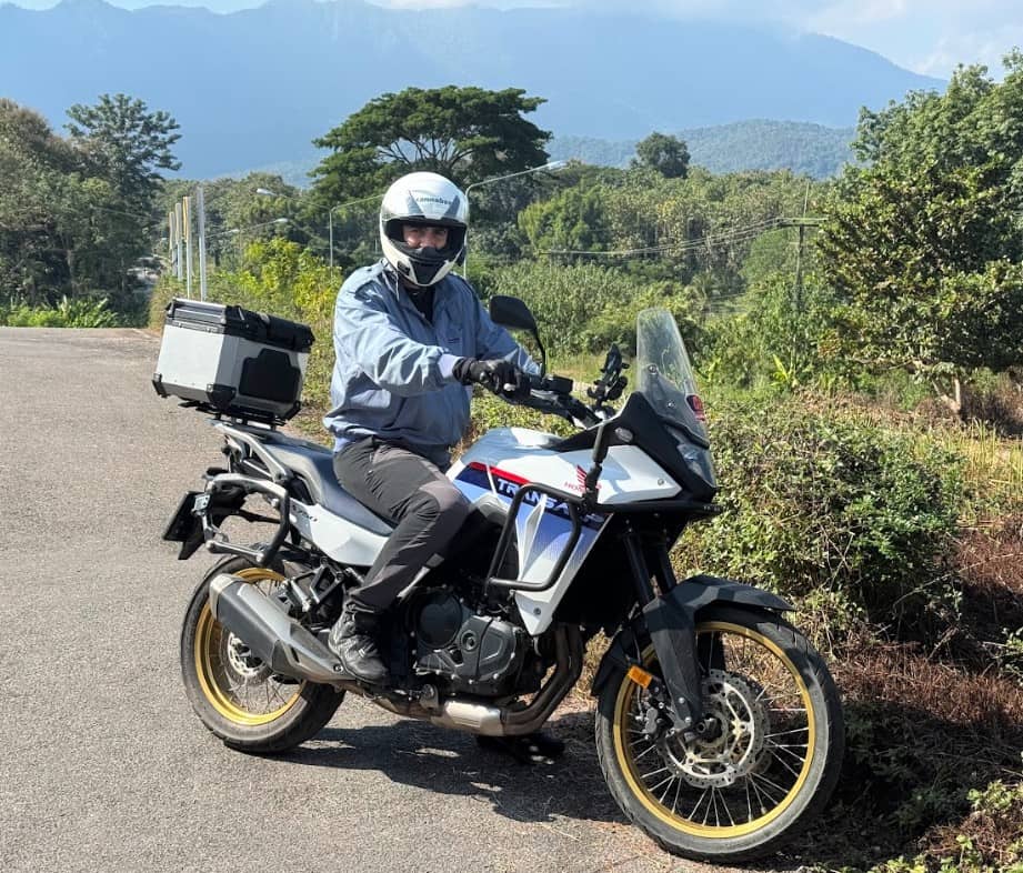 Motorcyclist wearing Pando Moto Skin UH AAA Leggings on a Honda Transalp, riding in a lush rural area with mountains in the background