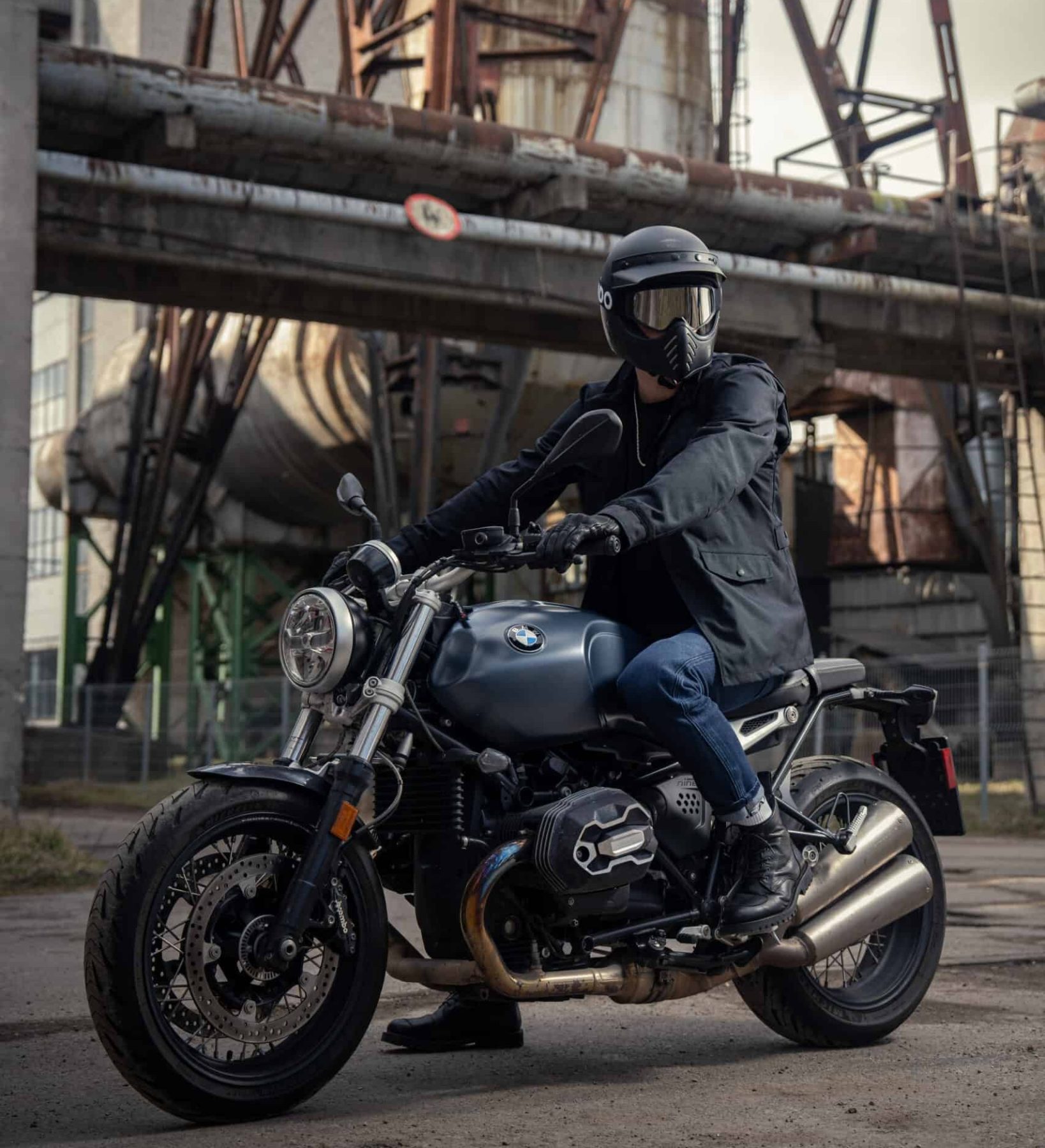 Street rider in urban gear on a BMW motorcycle near an industrial backdrop