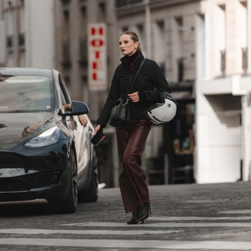 Woman in REV'IT! Rosier H2O jacket walking in the city crosswalk, holding a white helmet, blending casual style with motorcycle function.