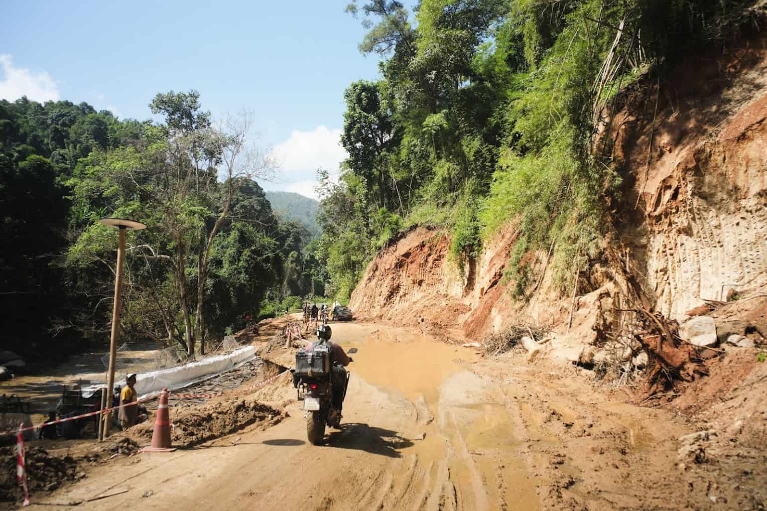 Adventure rider approaches a muddy, waterlogged mountain road—testing the waterproof performance of dual-sport gear.