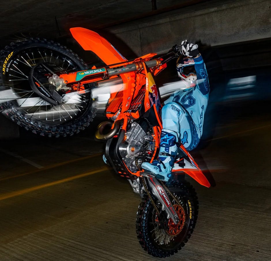 Rider performing a wheelie on a motocross bike in full MX gear