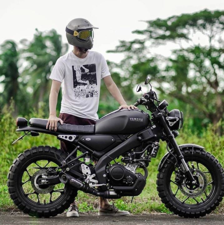 Man standing next to a Yamaha motorcycle fitted with aggressive knobby Shinko 804/805 Big Block tires on a road near greenery