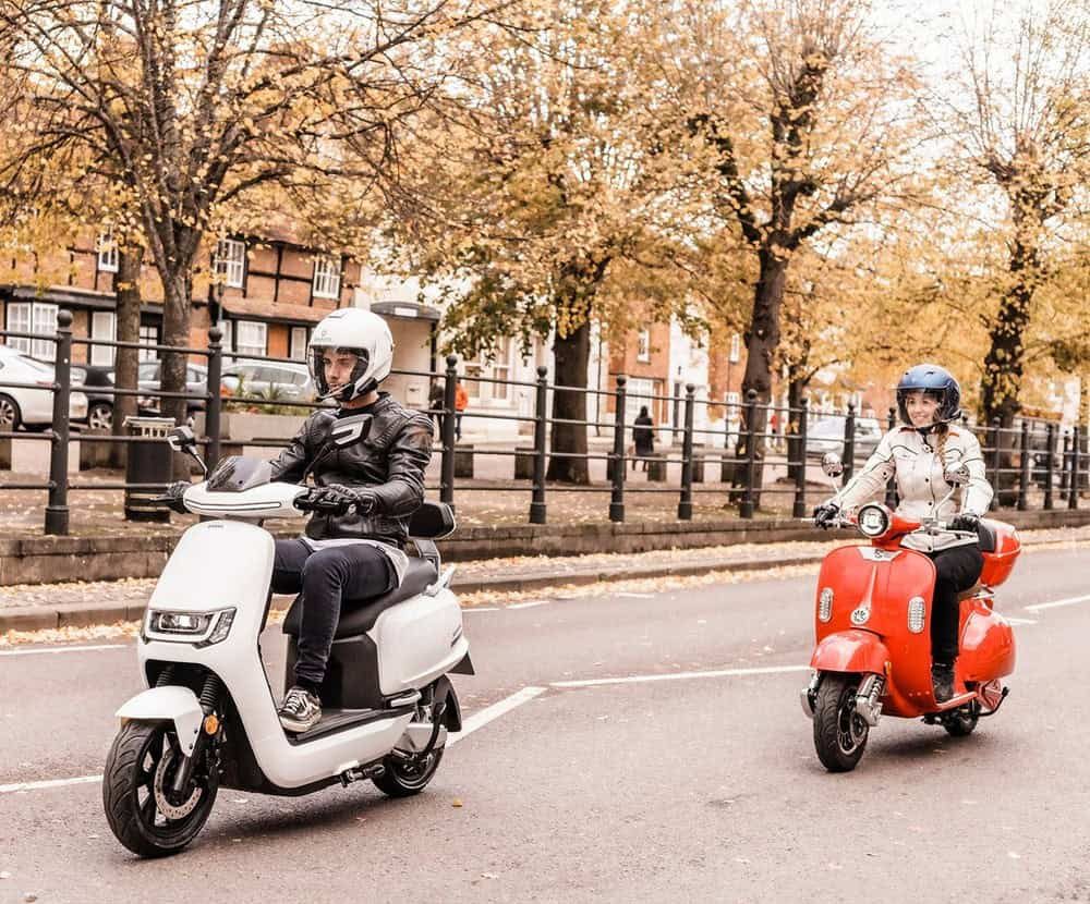 Two riders on scooters cruising through the city during autumn