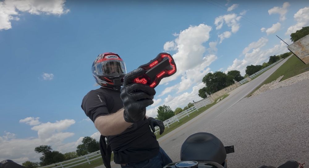 Motorcyclist holding up an illuminated Brake Free helmet light in daylight