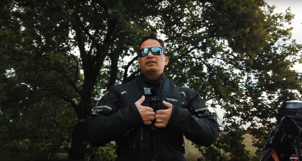 Rider adjusting the front buckles of the Helite E-Turtle vest, standing outdoors in full summer riding gear