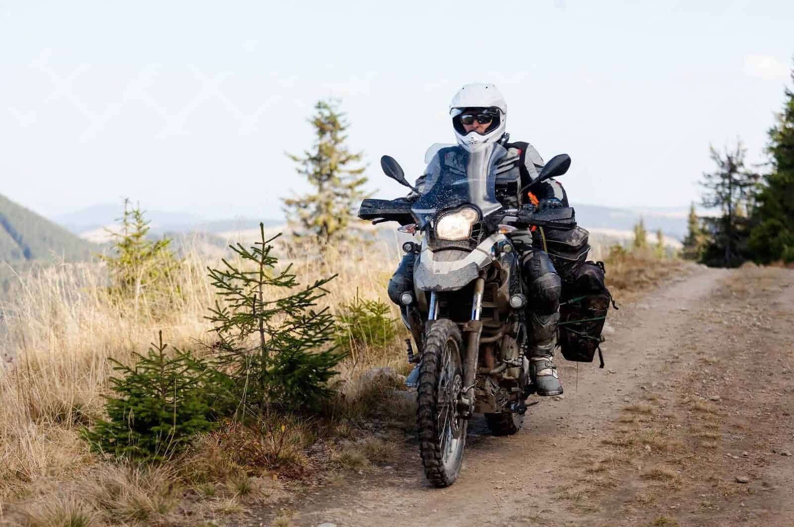 ADV rider with loaded gear navigating a dirt trail through mountain forest