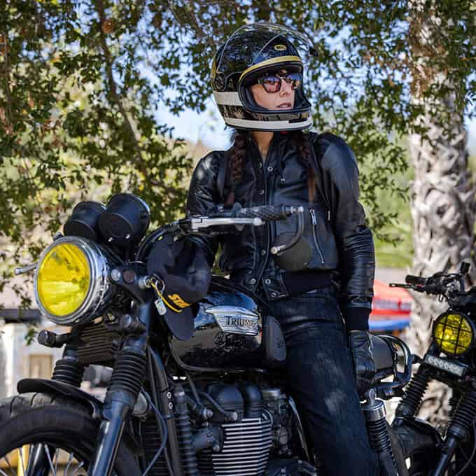 Female motorcyclist wearing sunglasses and a full-face helmet while sitting on a Triumph motorcycle.